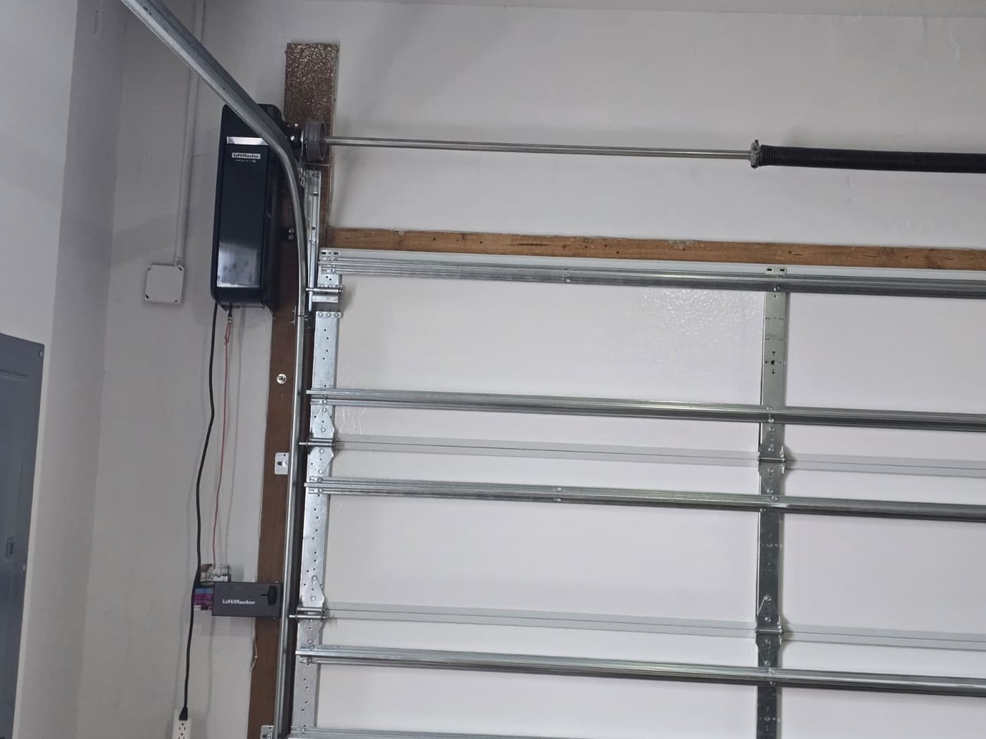 A garage door opener mounted to the ceiling of a garage with its rail running back to the top of the door.