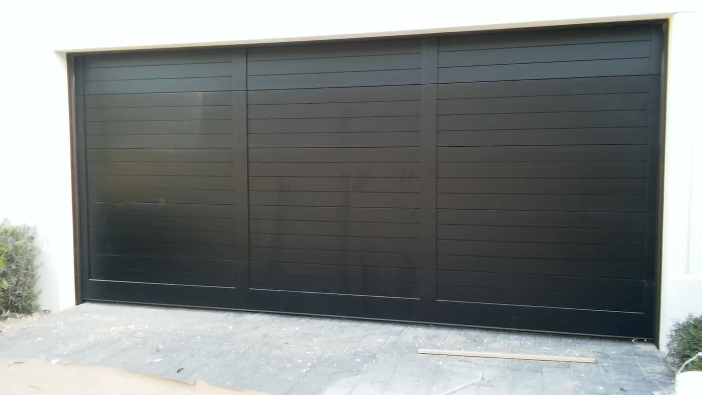 A wide, flush matte-black garage door with fine horizontal lines and no windows, set in a pale wall.